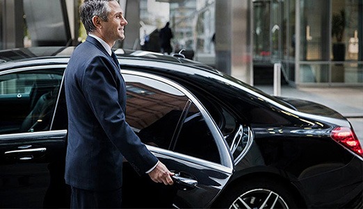 A sentura chauffeur helping a designated cooperate client out of a prestige car